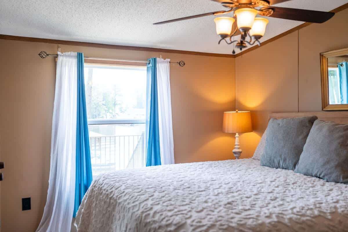 Een slaapkamer met een bed, een plafondventilator, een raam met gordijnen en een nachtkastje met een lamp.