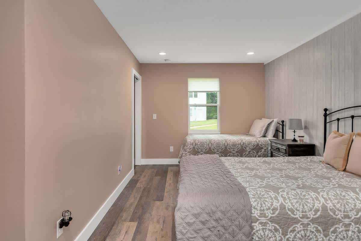 A bedroom with two beds, a window, and a nightstand with a lamp.