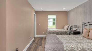 A bedroom with two beds, a window, and a nightstand with a lamp.
