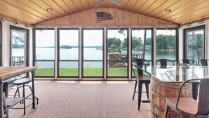 Un espacio al aire libre cubierto con una mesa, sillas, ventanas amplias y un ventilador de techo.
