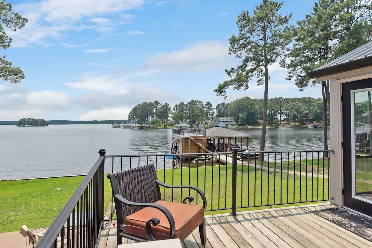 A wooden deck with a chair and a small table, overlooking a lake with a gazebo and a dock.