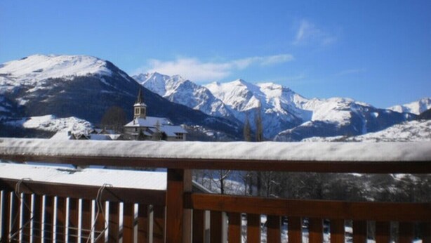 A mountain landscape with snow-covered peaks and a small building in the foreground.
