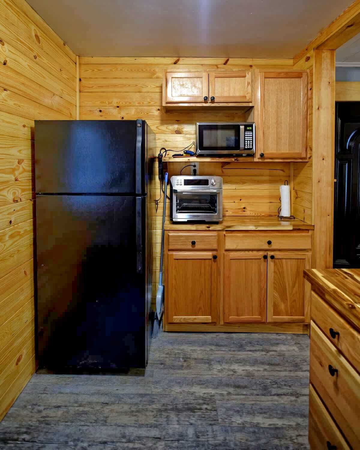 Une cuisine de taille réduite, dotée de meubles en bois, d’un réfrigérateur noir, d’un four à micro-ondes et d’un four traditionnel.