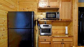 Une cuisine de taille réduite, dotée de meubles en bois, d’un réfrigérateur noir, d’un four à micro-ondes et d’un four traditionnel.