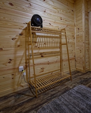 Una estantería de madera con un ventilador encima, un enchufe y una alfombra gris en el suelo.