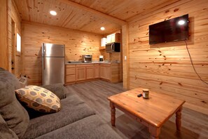 A cozy cabin interior with a wooden interior, a sofa, a table, a TV mounted on the wall, and a kitchen area.
