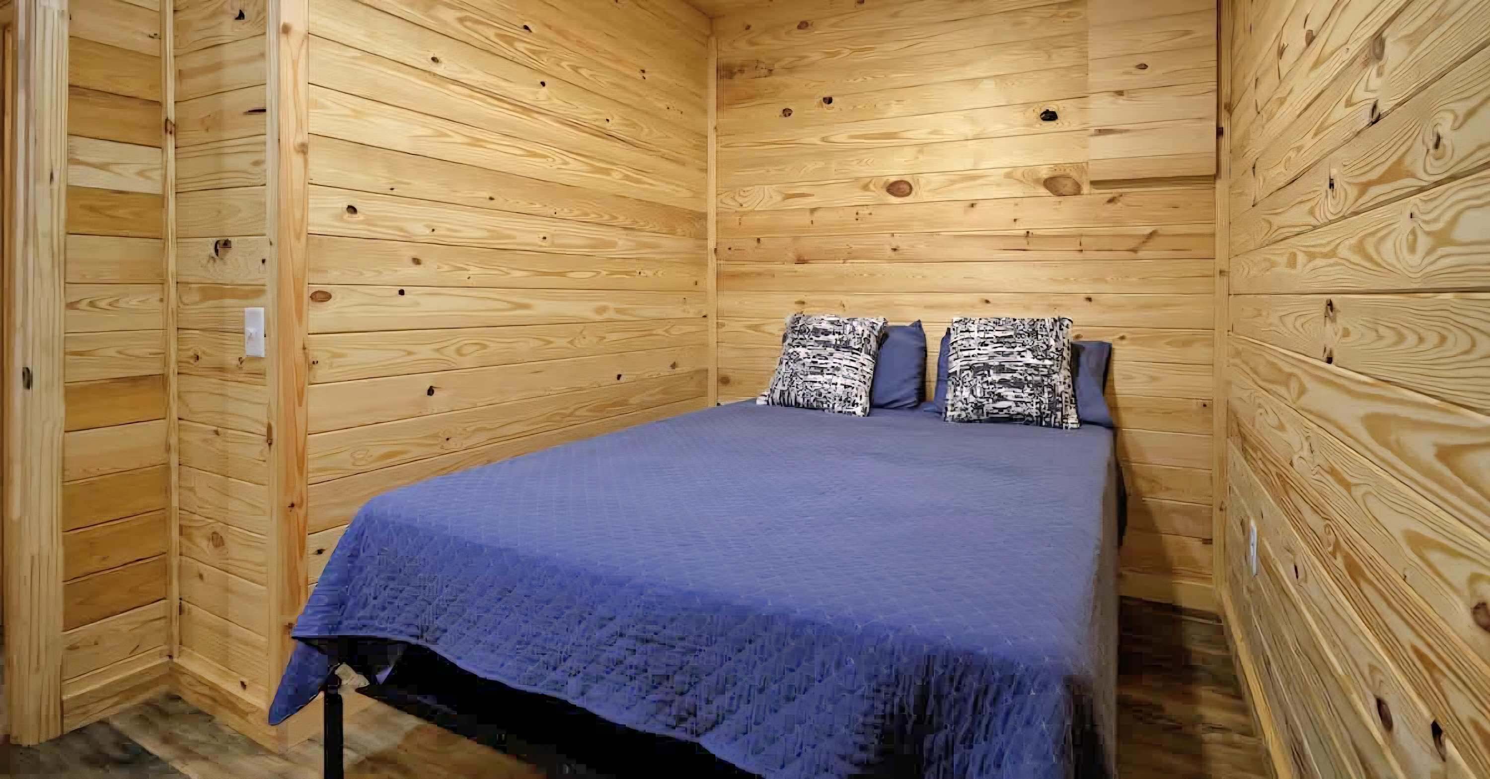 Une pièce aux murs lambrés, avec un lit, des oreillers et une couverture.