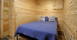 Una habitación con paneles de madera, una cama, almohadas y una manta.