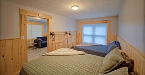 Une pièce avec deux lits, des murs en bois, une fenêtre et une porte donnant sur une autre pièce.