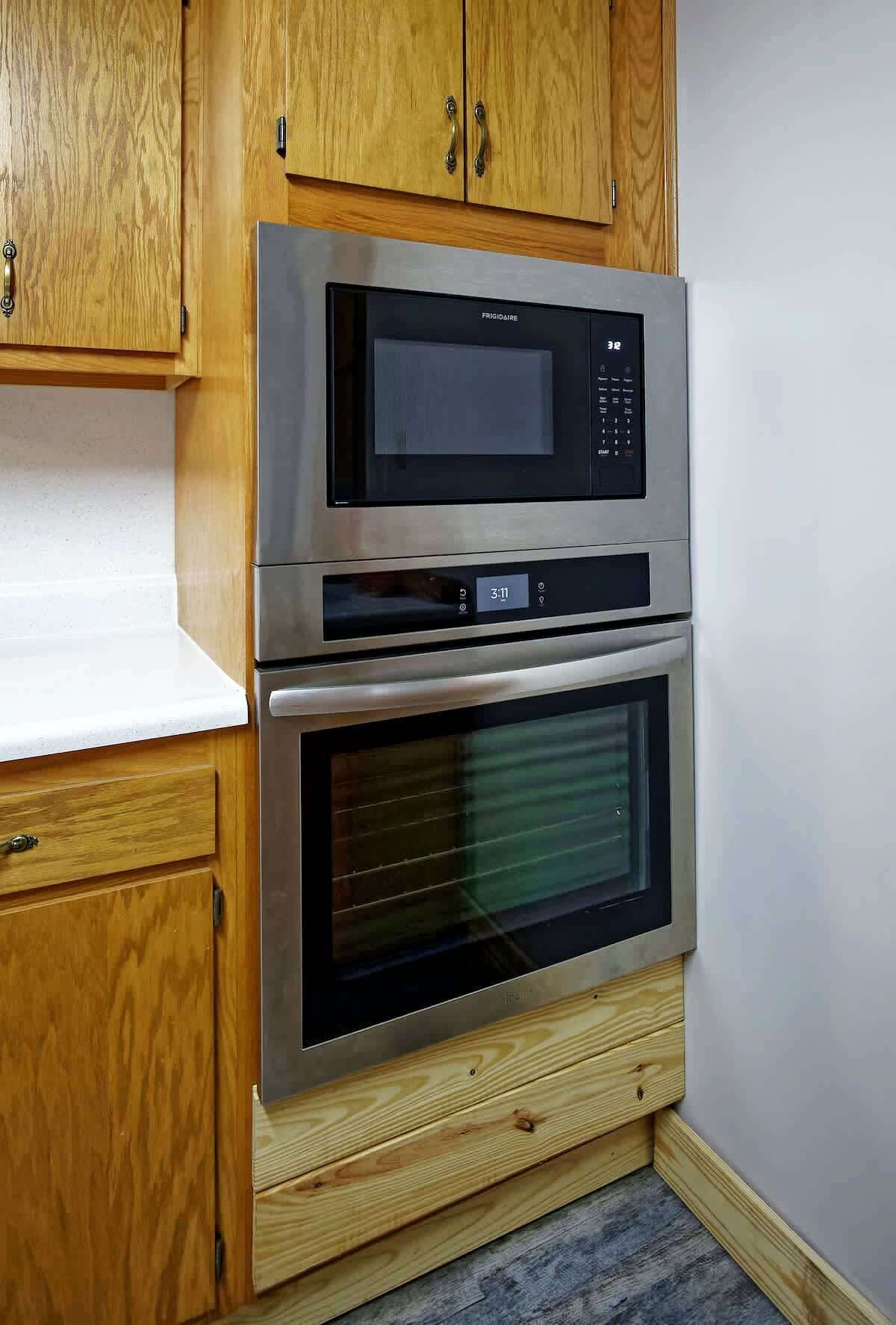 A kitchen with a built-in microwave and oven, wooden cabinets, and a white countertop.