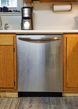 A stainless steel dishwasher in a kitchen with wooden cabinets and a window above the sink.