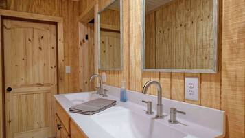 A wooden cabin bathroom with a double sink, two mirrors, and a door.