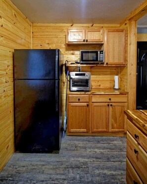 A compact kitchen with wooden cabinets, a black refrigerator, a microwave, and an oven.