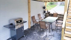 Un espacio al aire libre techado con una parrilla, una mesa con sillas y vistas a un área verde.