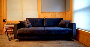 Un canapé de couleur sombre avec deux coussins, une petite table avec une chaise et un radiateur fixé au mur.