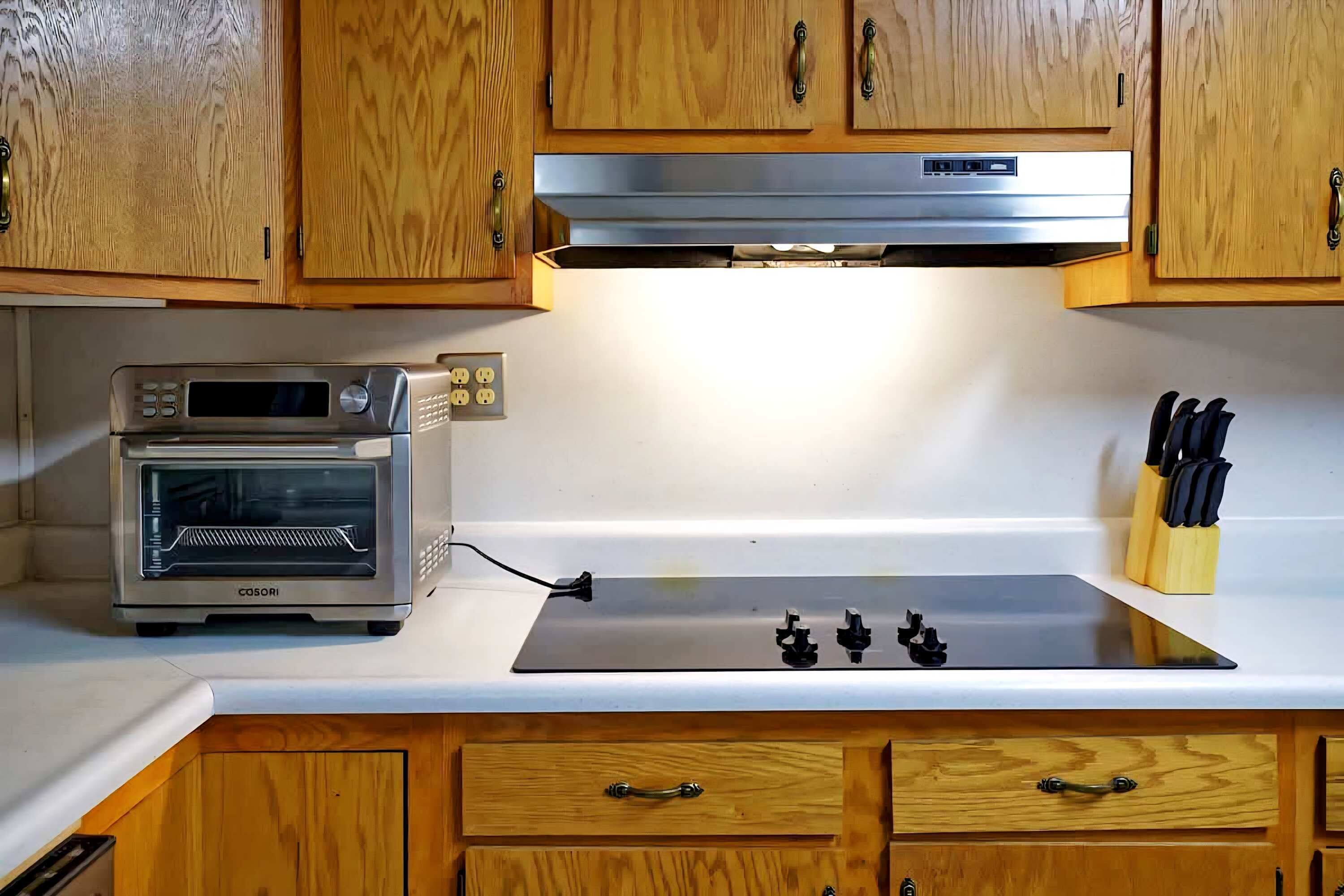 A kitchen with wooden cabinets, a built-in microwave, a stovetop, and a knife block.
