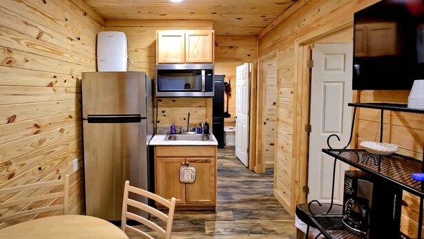 Una cocina compacta con paredes de madera, un refrigerador, microondas y un lavamanos.