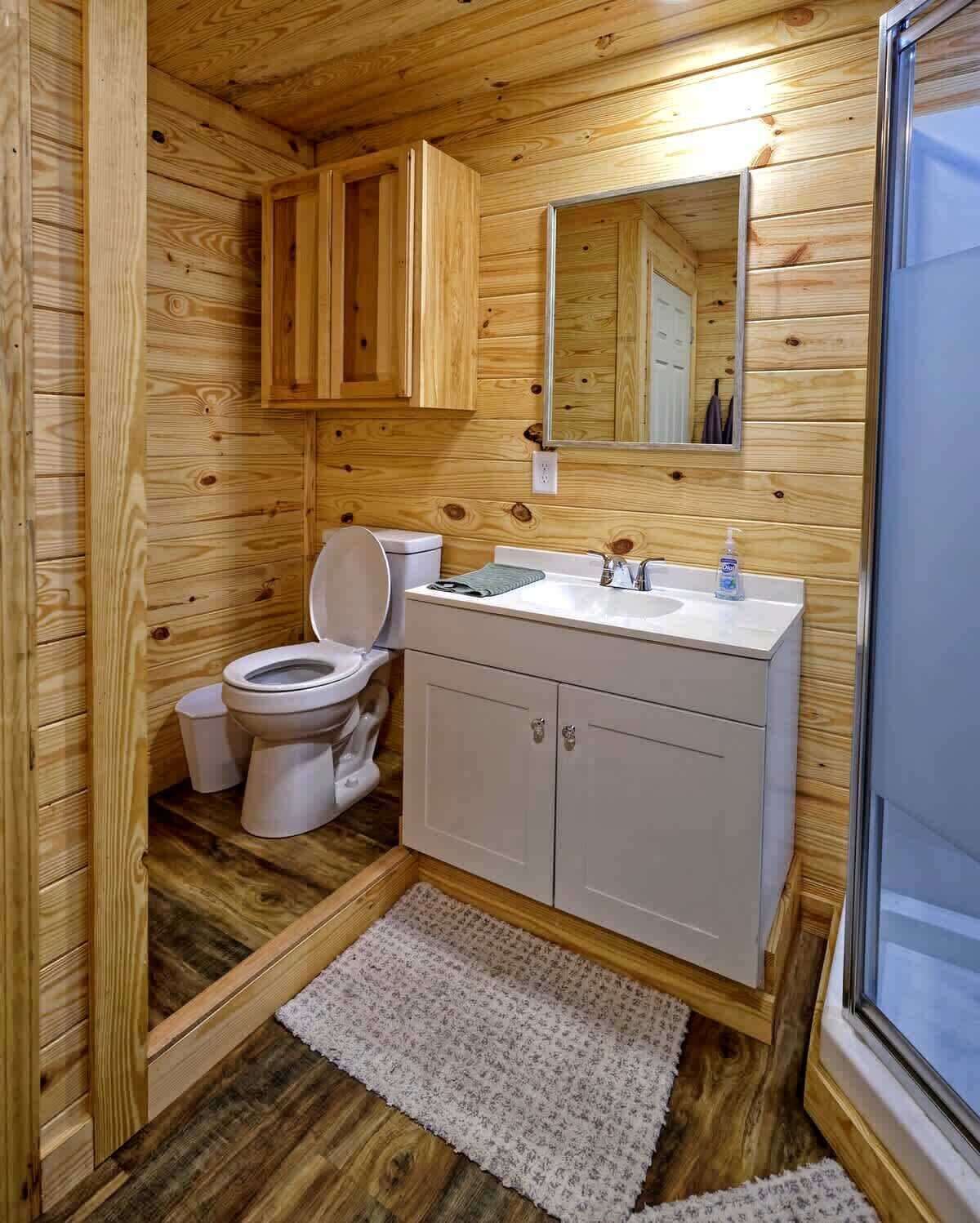 A wooden-paneled bathroom with a toilet, sink, and cabinets.