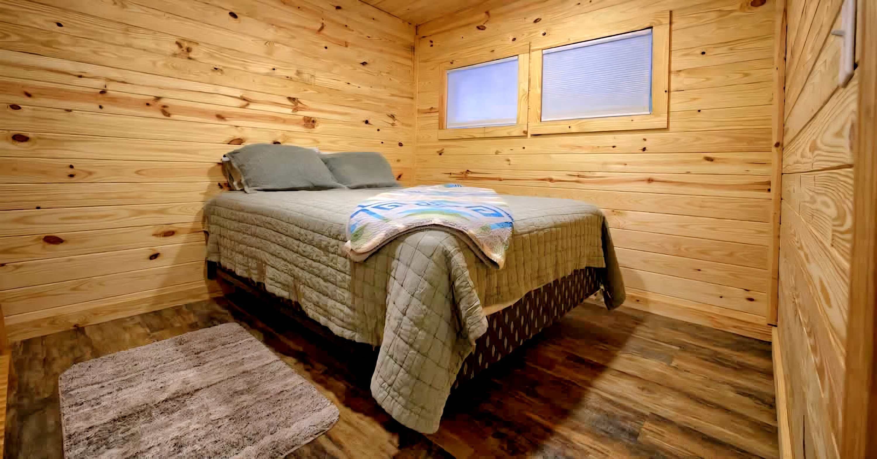 A wooden cabin bedroom with a bed, pillows, a blanket, and a rug.