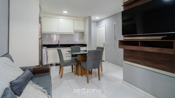 Un espace de vie compact comprenant un coin repas, une kitchenette et un téléviseur à écran plat fixé au mur.