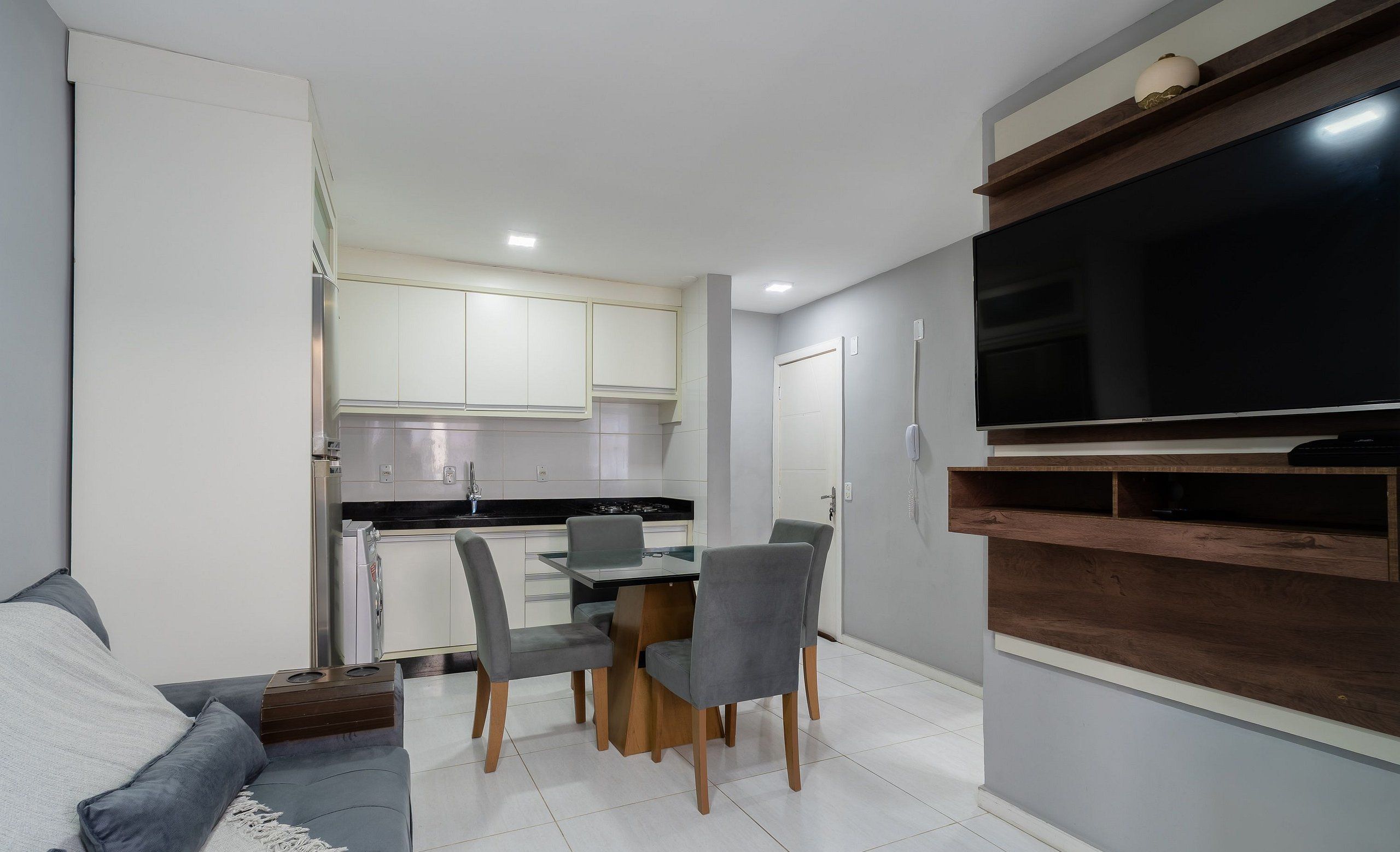 A compact living space with a dining area, kitchenette, and a flat-screen TV mounted on the wall.