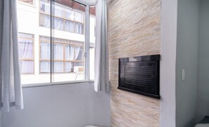 A room with a large window, a stone wall, and a black air conditioning unit. - Apartments in a Building 500m From Canasvieiras Beach - Gals (Florianópolis)
