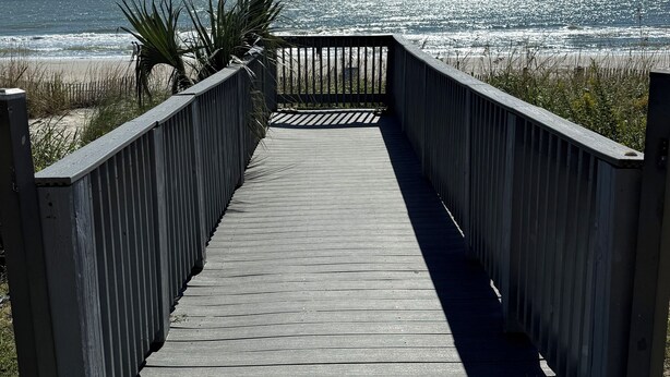 Ein hölzerner Steg führt zu einem Strand mit freiem Blick auf den Ozean.