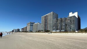 Ein Strand mit hoch aufragenden Gebäuden, Sandstrand und blauem Himmel.