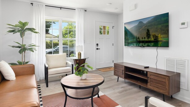 A modern living room with a sofa, a round table, a TV, and a large window. - Stylish Queen City Getaway in Camp North End (Charlotte)