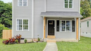 A two-story house with a front porch, a driveway, and a well-maintained lawn. - Stylish Queen City Getaway in Camp North End (Charlotte)