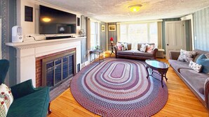 A living room with a fireplace, a television, a sofa, and a patterned rug. - Pet-Friendly Cape Escape w/ Firepit & Beach Access (Harwich)