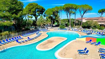 A swimming pool with blue lounge chairs and a sandy area, surrounded by trees and buildings.