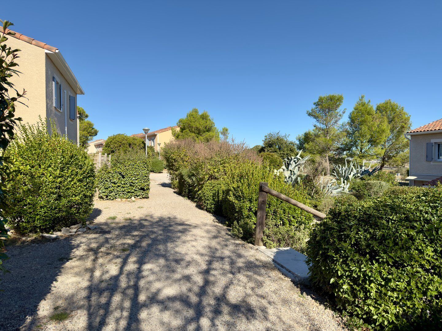 A gravel pathway leading to a building with a tiled roof, surrounded by well-maintained hedges and trees.