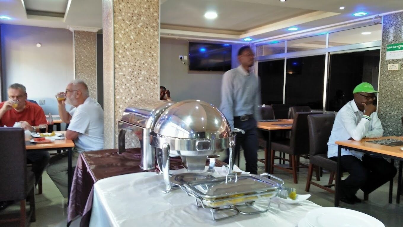 A buffet setup with a large metal serving dish in the center, surrounded by tables with people dining.