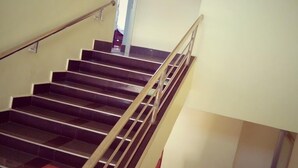 Una escalera con barandilla, escalones de madera y un rellano con baldosas rojas.