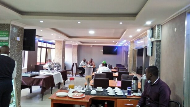 Un área de comedor con mesas dispuestas para el desayuno, una barra de buffet y una pantalla de televisión en la pared.
