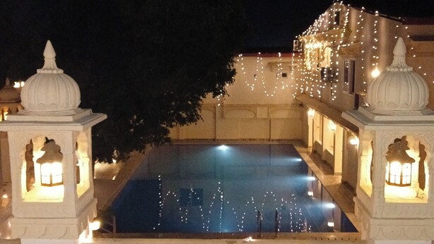 A nighttime view of a pool with decorative lighting, surrounded by ornate structures with lanterns. - Udai Nature Valley Resort Udaipur (Udaipur)
