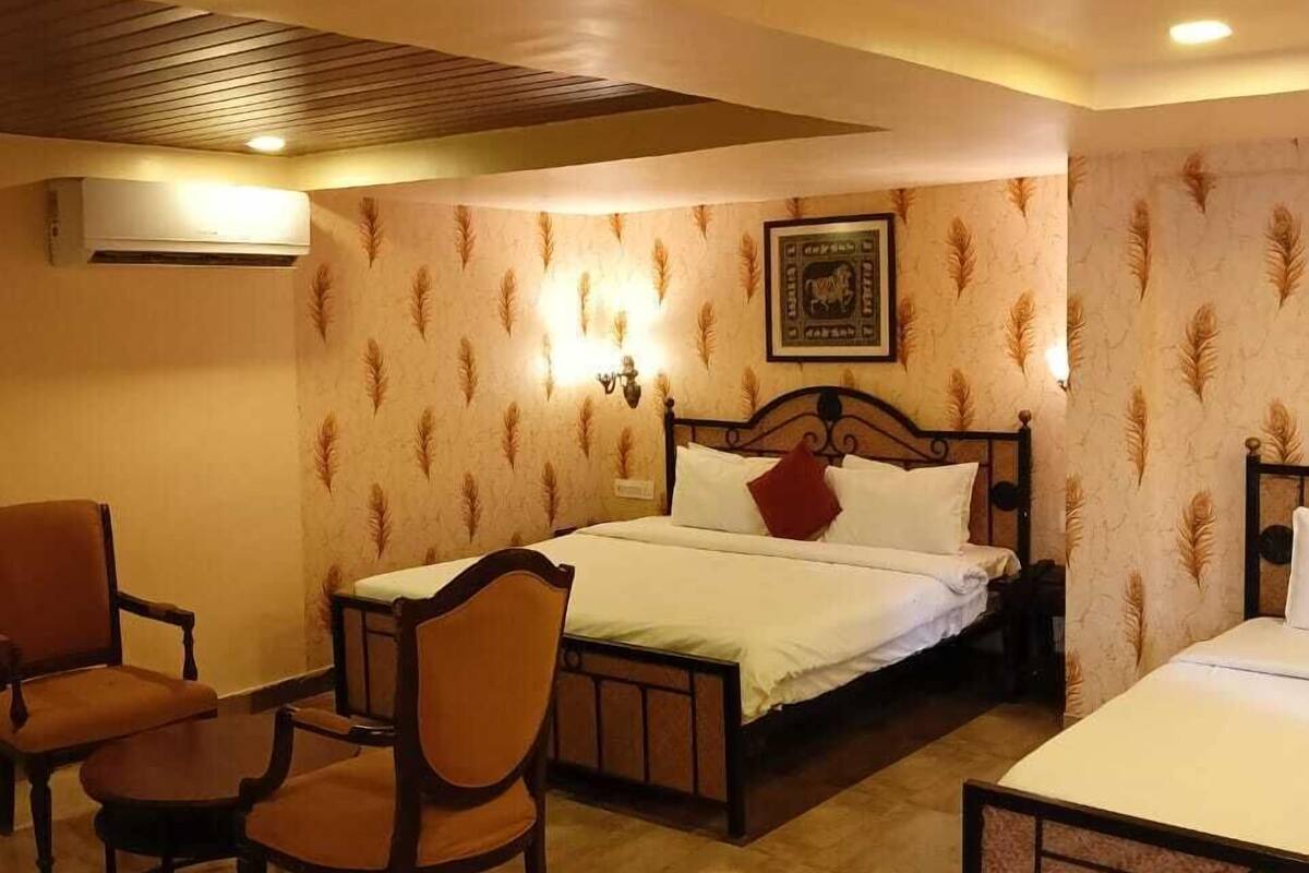 A hotel room with a bed, two chairs, a small table, and a wall-mounted air conditioner.