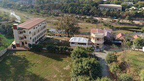 A large building with multiple floors and a flat roof, surrounded by greenery and a river. - Udai Nature Valley Resort Udaipur (Udaipur)
