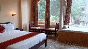 A hotel room with a bed, a dining table with chairs, a window with curtains, and a ceiling fan. - Udai Nature Valley Resort Udaipur (Udaipur)