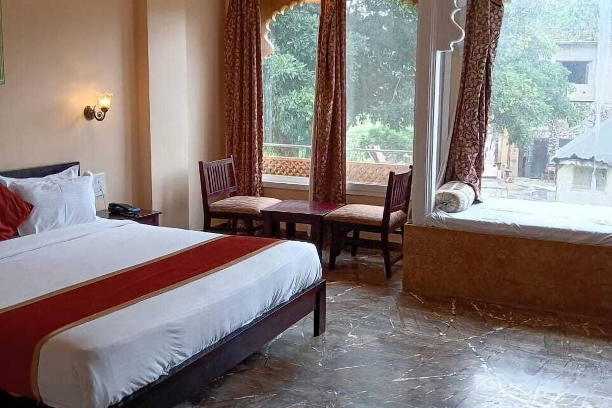 A hotel room with a bed, a dining table with chairs, a window with curtains, and a ceiling fan.
