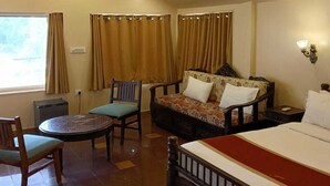 A hotel room with a bed, a sofa, two chairs, a small table, a ceiling fan, and a window with curtains. - Udai Nature Valley Resort Udaipur (Udaipur)