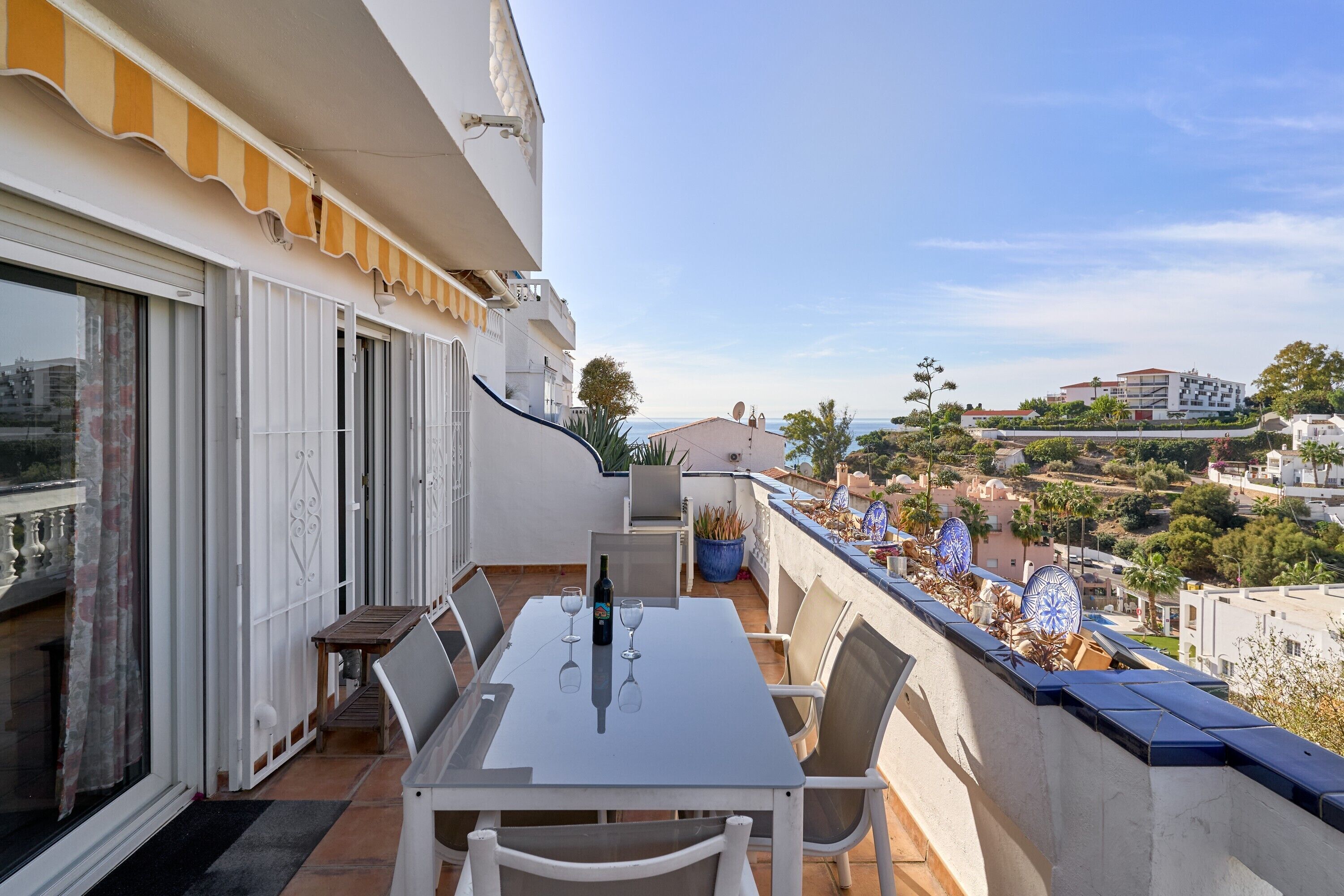 A balcony with a table and chairs, a bottle, and wine glasses.