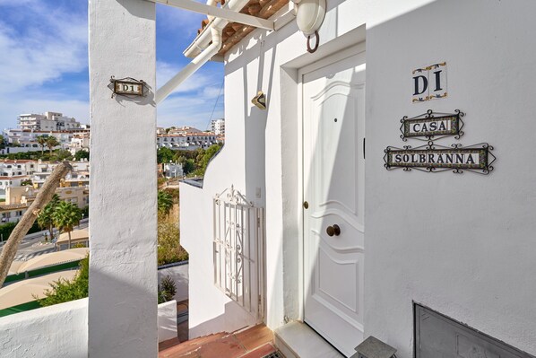 A white building with a balcony, a door, and a window. There are signs on the wall that read 'DI CASA SOLBRANNA'.