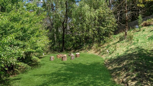 Un área cubierta de césped con varias estructuras de madera, rodeada de árboles frondosos y una valla de madera.