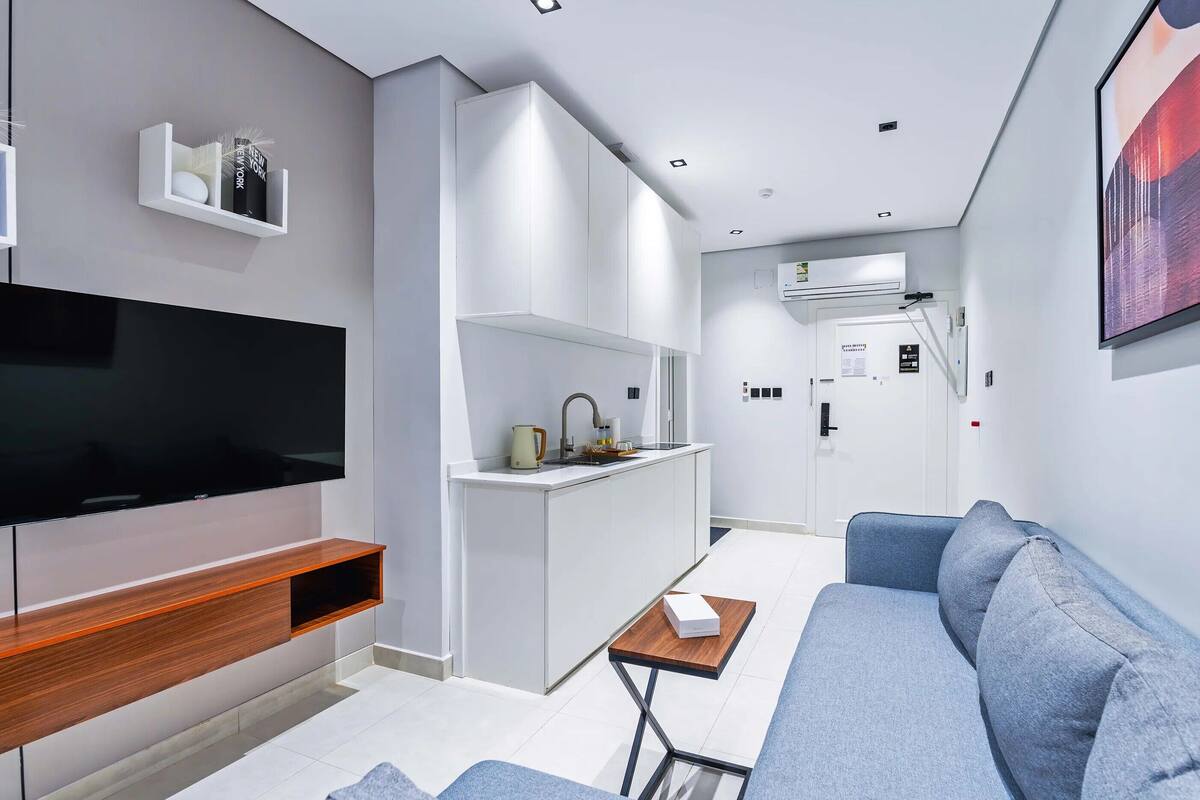 A modern living room with a flat-screen TV, grey sofa, and a small wooden table.