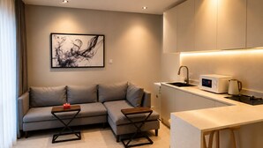Ein modernes Wohnzimmer mit einer Couch, einem kleinen Couchtisch, einer Küchenzeile mit Mikrowelle und Spüle.