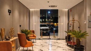 Eine Lobby mit Marmorboden, einem Empfangstresen, orangefarbenen Stühlen und Blick auf geparkte Autos vor dem Haus.