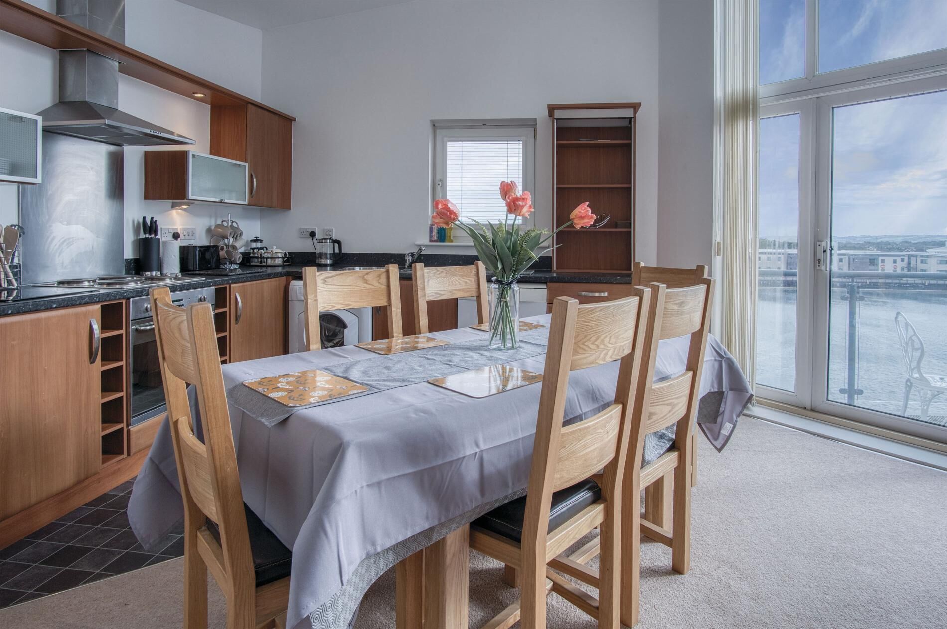 A modern kitchen with wooden cabinets, a stainless steel range hood, and a dining area with a table set for four.