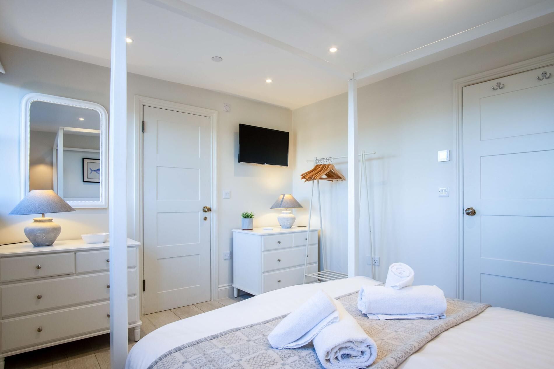 Ein Hotelzimmer mit Bett, Schminktisch, Wandfernseher und Kleiderhaken mit Kleiderbügeln.
